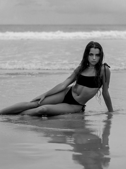 Model wearing the Maui black bikini top and Lolani tie bottom in a sunny beach setting